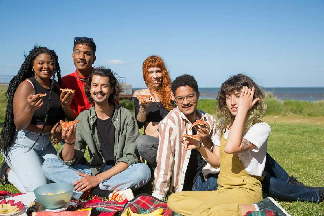 A group of friends enjoying pizza on a picnic A group of friends enjoying pizza on a picnic