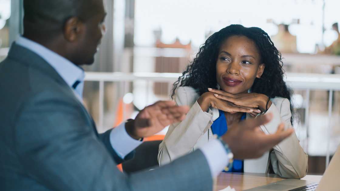 Two people in business attire talk at a table. Two people in business attire talk at a table.
