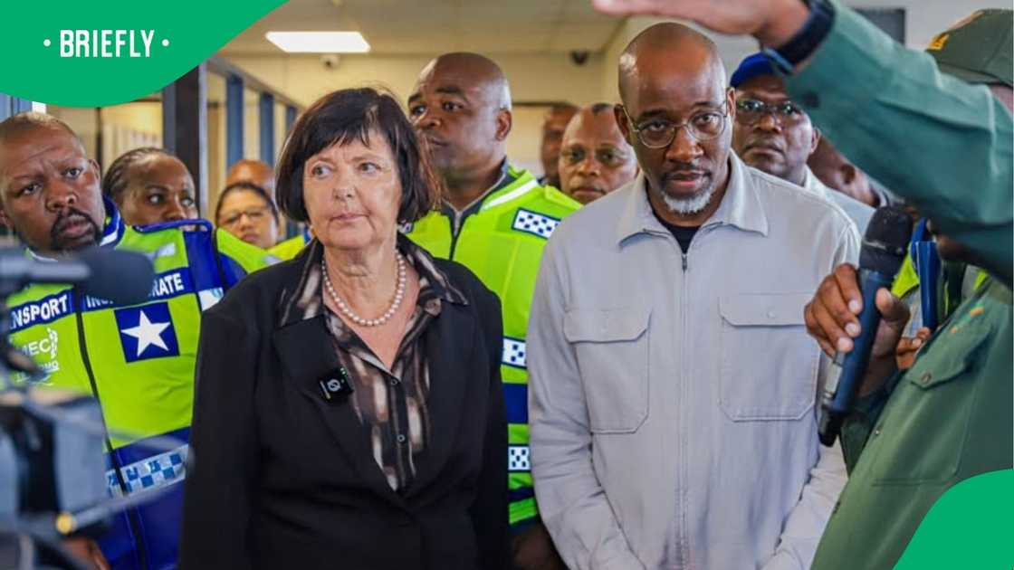 The minister stood alongside colleagues and security personnel in high-visibility uniforms as someone spoke into a microphone The minister stood alongside colleagues and security personnel in high-visibility uniforms as someone spoke into a microphone