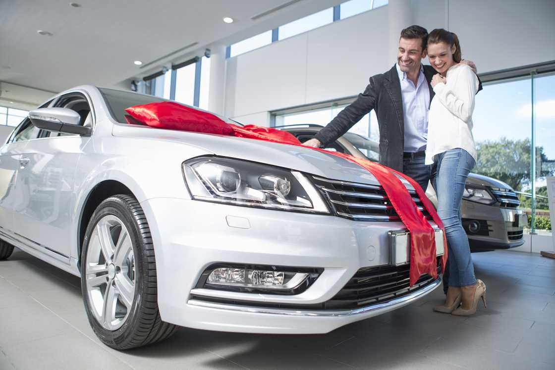 A man looked at a new car with red bow with girlfriend in car dealership