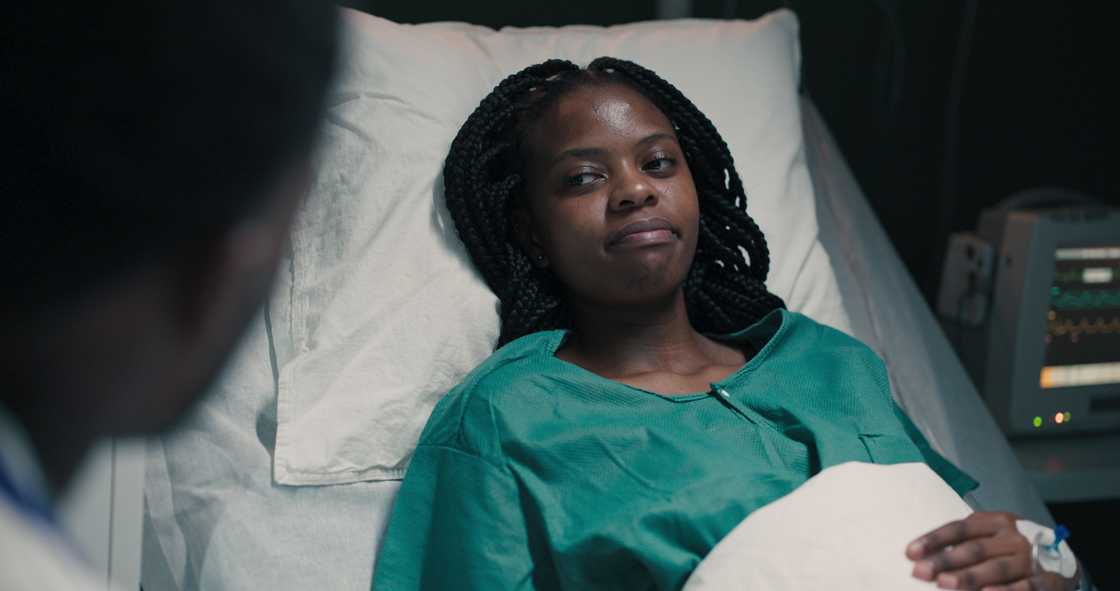 Young African doctor sits beside a patient's bedside in the hospital room.