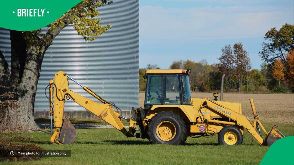 A yellow TLB parked on the grass. A yellow TLB parked on the grass.