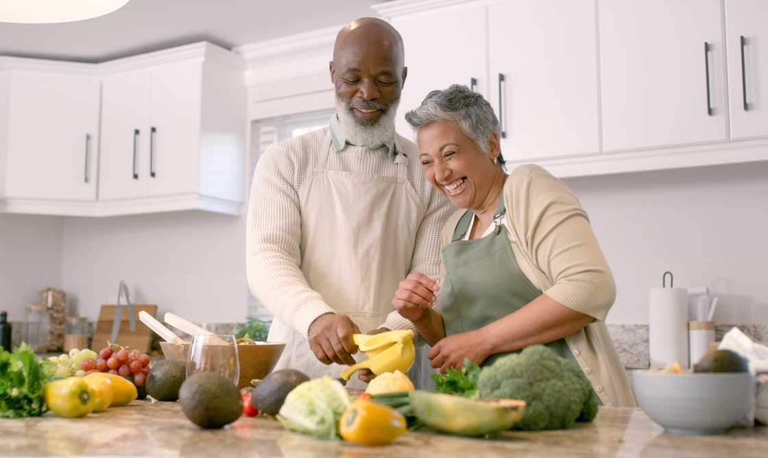 A couple laughing while preparing a meal together in their house.