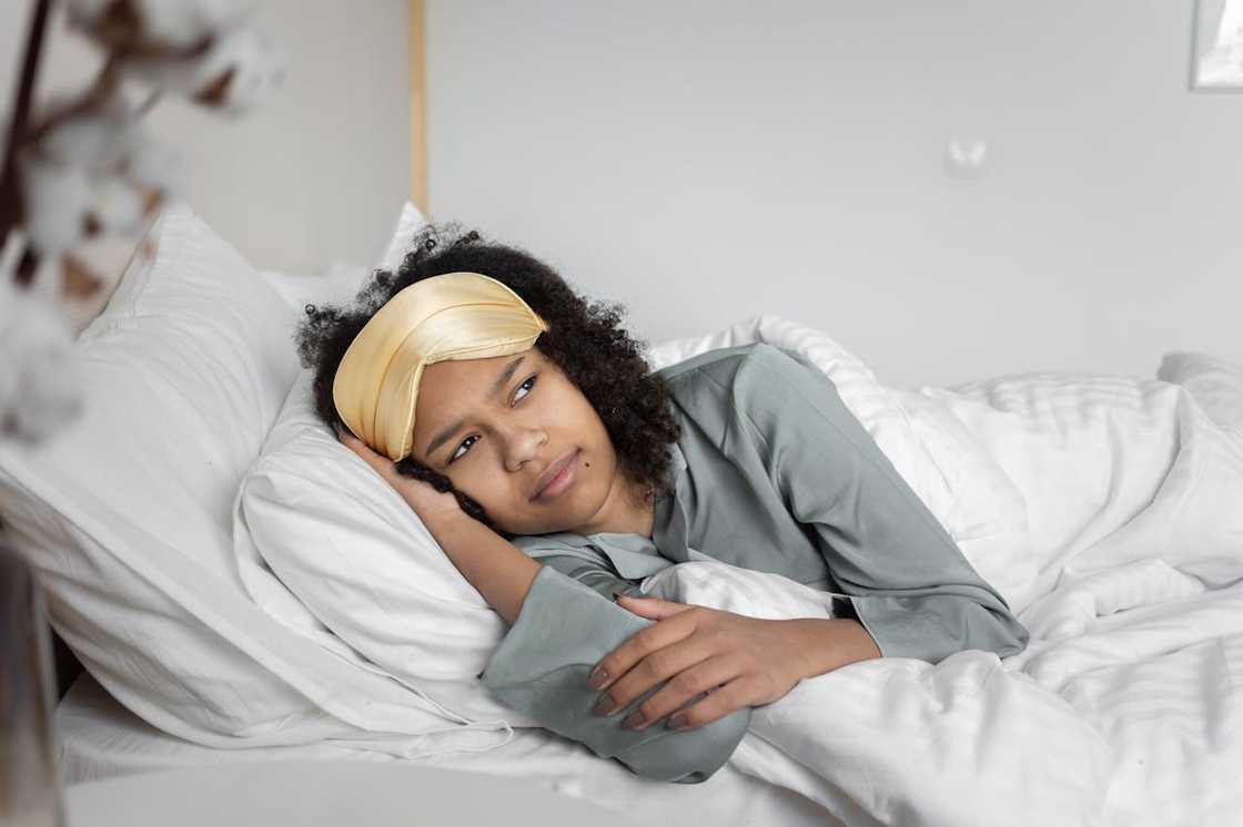 A young woman lying awake in bed wearing a sleep mask, looking thoughtful and restless. A young woman lying awake in bed wearing a sleep mask, looking thoughtful and restless.