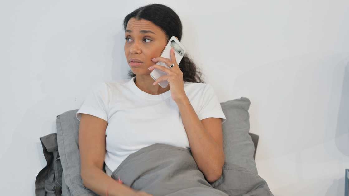 Woman on a phone call, expression calm but wounded, sitting on her bed. Woman on a phone call, expression calm but wounded, sitting on her bed.