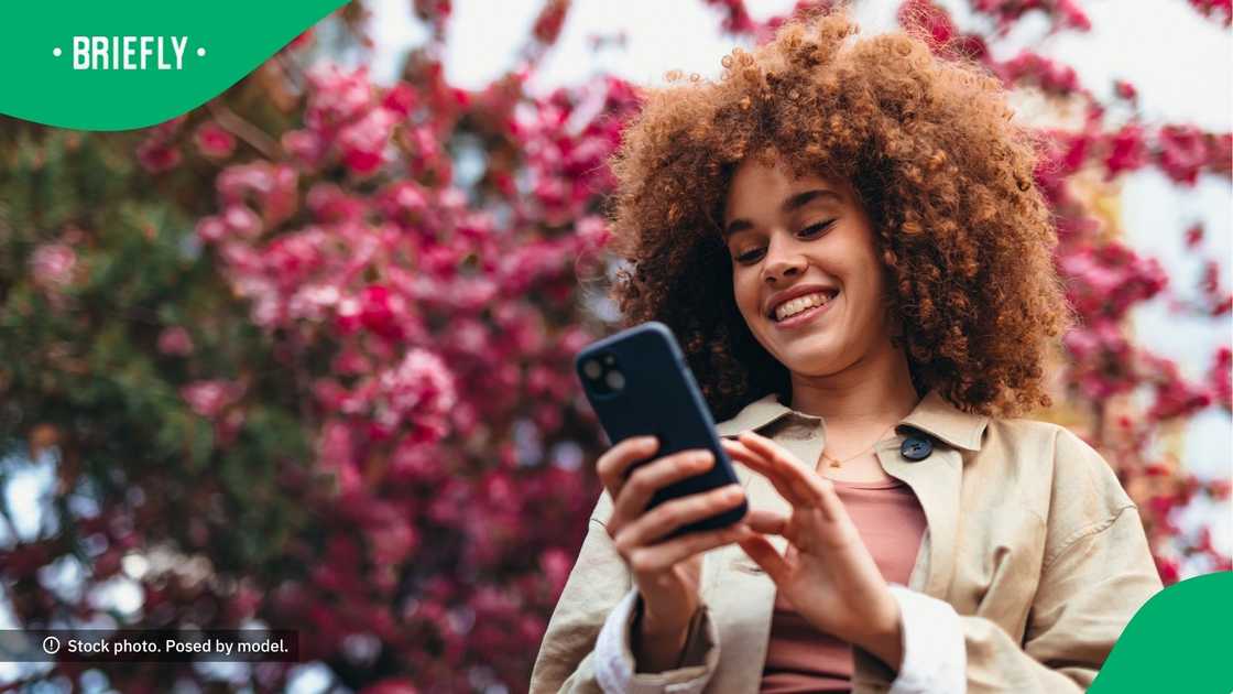 A curly-haired woman smiling at her phone. A curly-haired woman smiling at her phone.