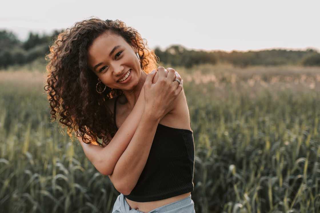 Smiling woman standing in a green field at sunset.