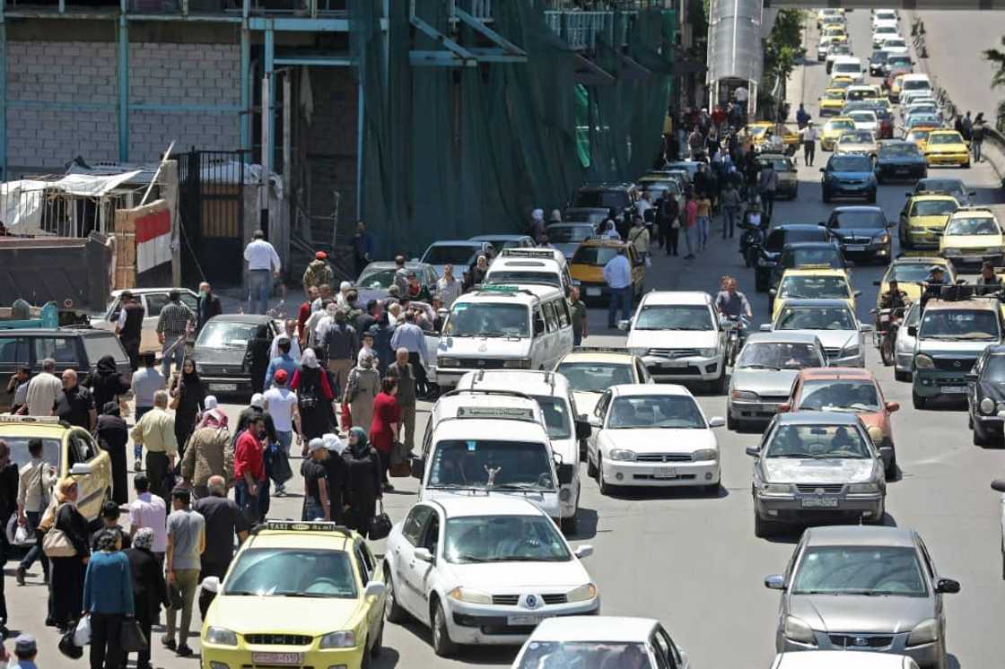 In this file photo taken on May 10, 2020, pedestrians walk along a line of cars in a busy street in the Syrian capital Damascus