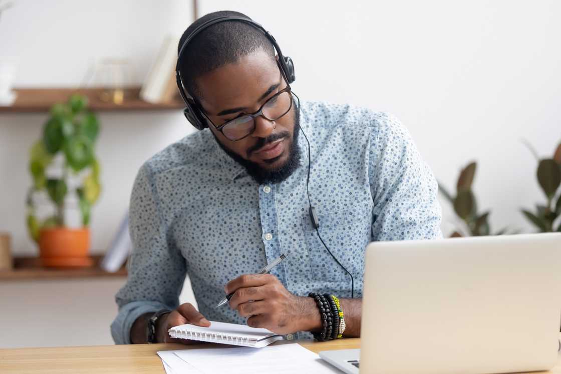 A businessman in headphones writing notes in a notebook.