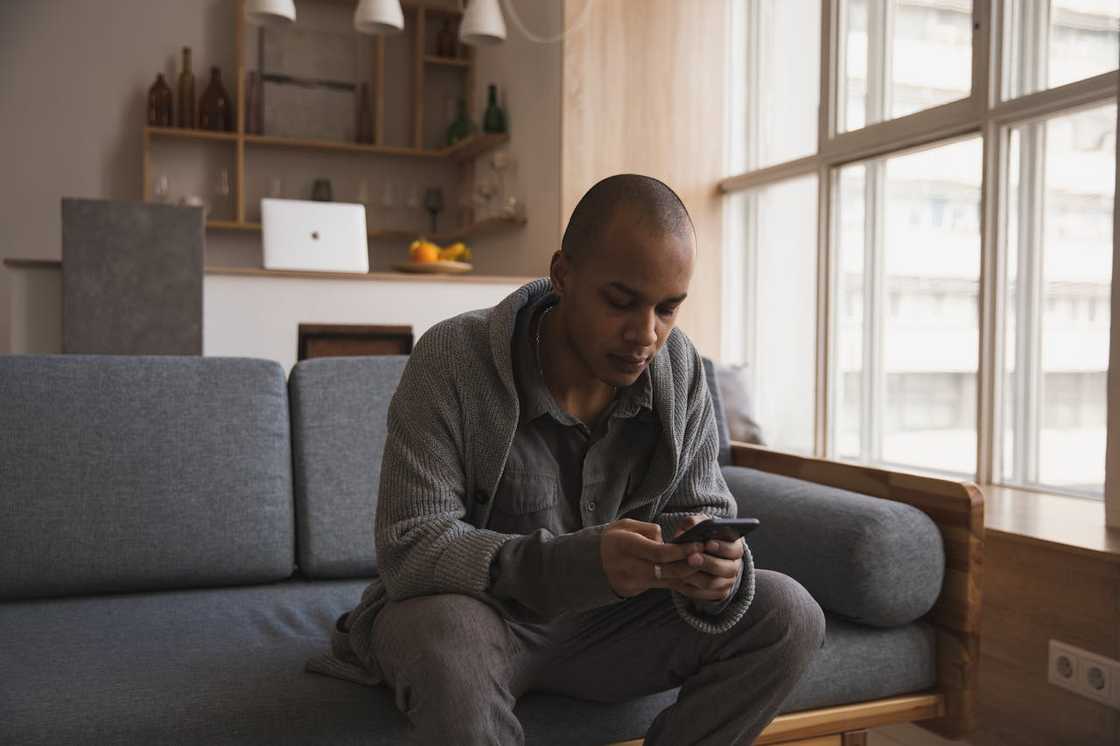A man sitting on a sofa, looking down at his phone. A man sitting on a sofa, looking down at his phone.