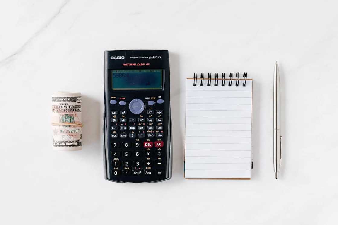 A bundle of notes, calculator, notebook and pen on a white surface