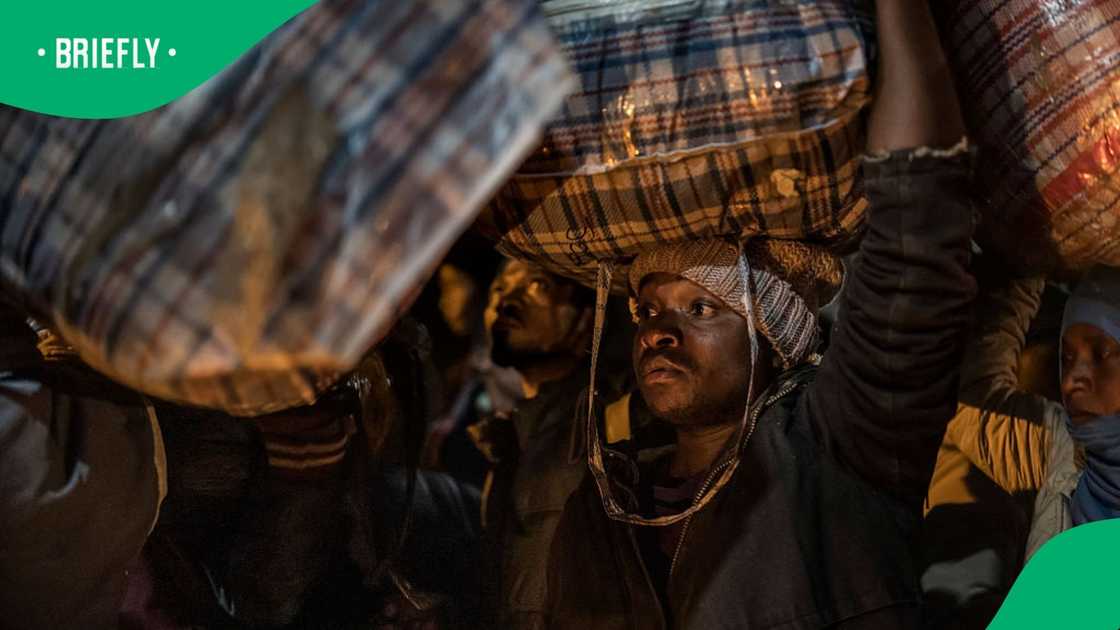 TOPSHOT - A Malawian migrant carries his belonging as he lines up to board a bus while gathering in front of the Malawian Consulate in Johannesburg, on July 14, 2026 ahead of their repatriation towards Malawi