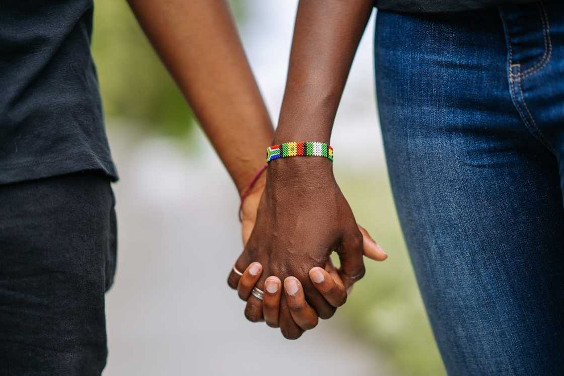 Close-up of two people holding hands outdoors.