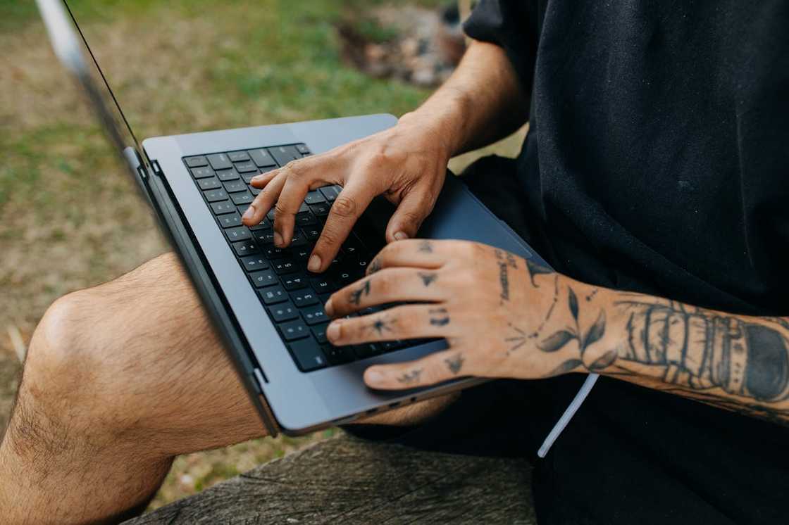 A man with tattooed hands types on a laptop.
