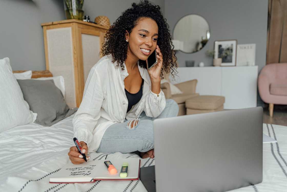 A woman smiling while talking on the phone and working on a laptop at home. A woman smiling while talking on the phone and working on a laptop at home.