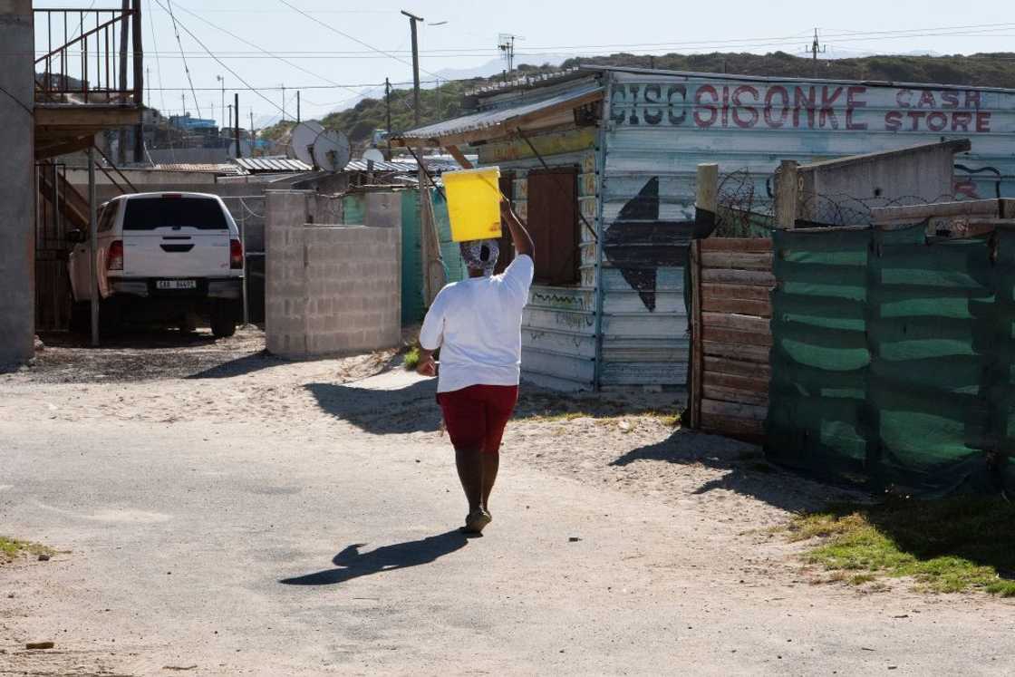 A woman carries a bucket of water which she filled at a local tap in Zwelitsha, an informal settlement in Khayelitsha that is home to millions of people in mostly impoverished circumstances, near Cape Town on February 24, 2022