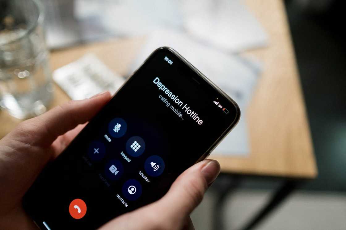 A person holds a smartphone showing a depression hotline call screen.