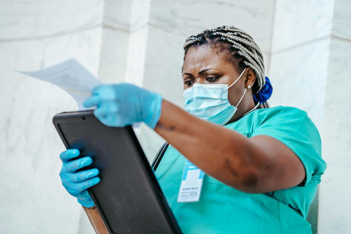 A female healthcare provider in scrubs and gloves is reading documents