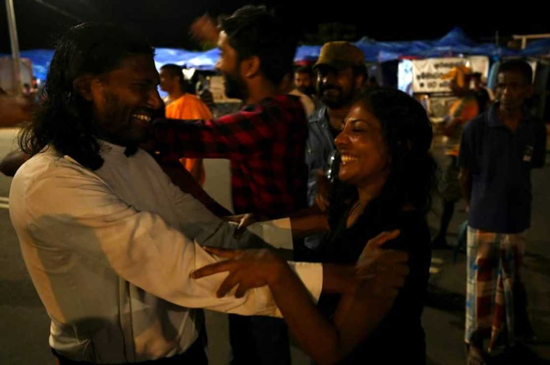 A stone's throw from what had days earlier been the office of President Gotabaya Rajapaksa, Sri Lankans smile wearily at their compatriots as they dance, hand out sweets, embrace each other or wave the national flag