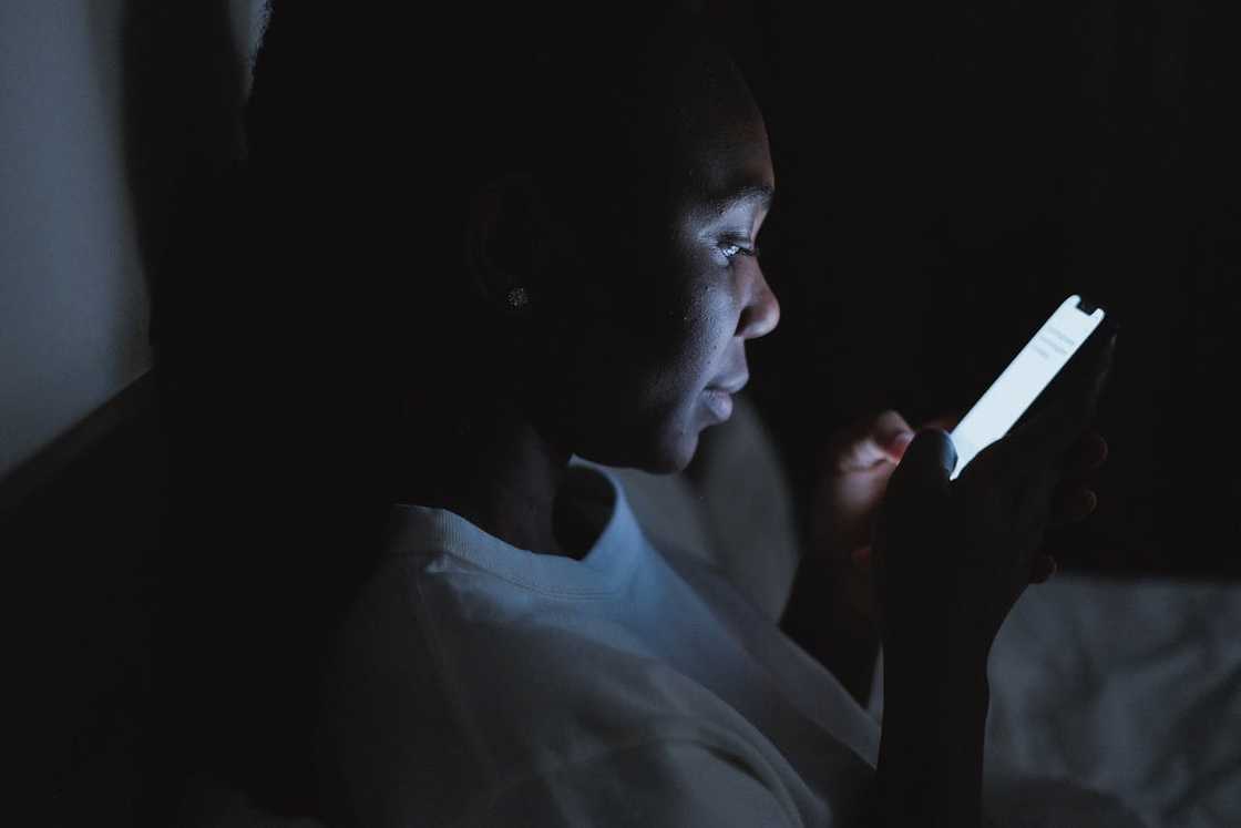 A woman sits in a dark room looking at her phone.
