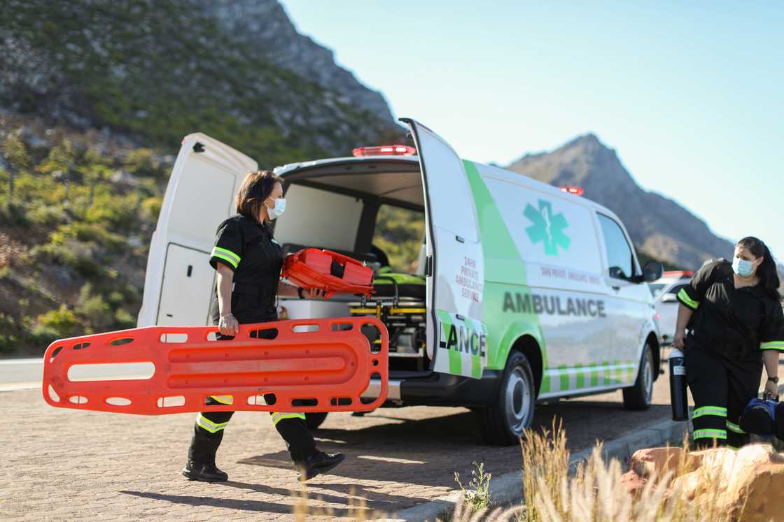 Two caucasian female paramedics wearing protective face masks carrying emergency equipment to an injured hiker on a hiking trial in the Helderberg, Gordon's Bay Two caucasian female paramedics wearing protective face masks carrying emergency equipment to an injured hiker on a hiking trial in the Helderberg, Gordon's Bay
