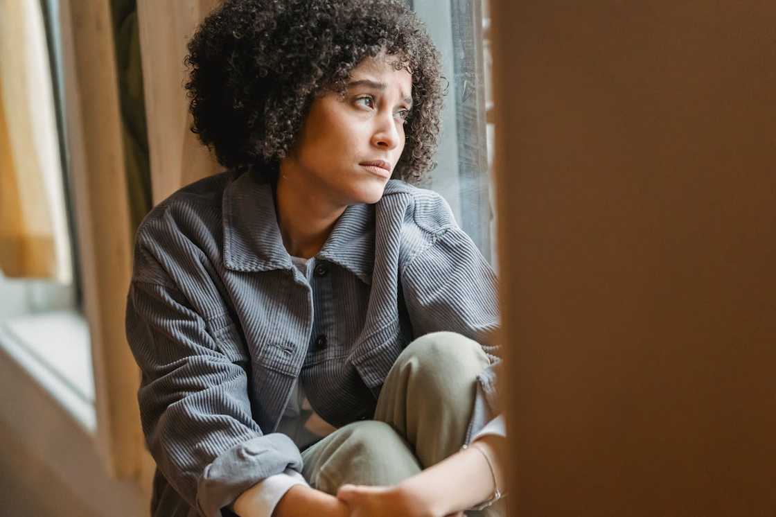 Woman sitting by a window, looking thoughtful and concerned. Woman sitting by a window, looking thoughtful and concerned.