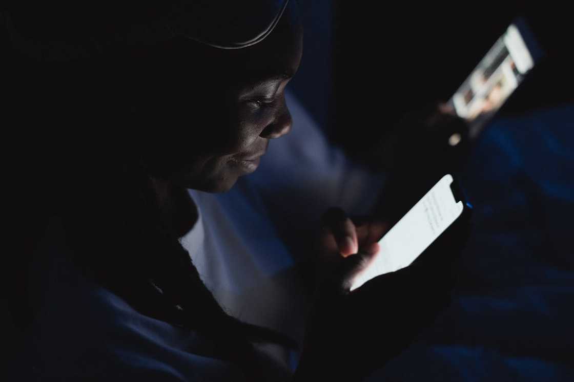 A person using a smartphone in a dark, low-light setting. A person using a smartphone in a dark, low-light setting.