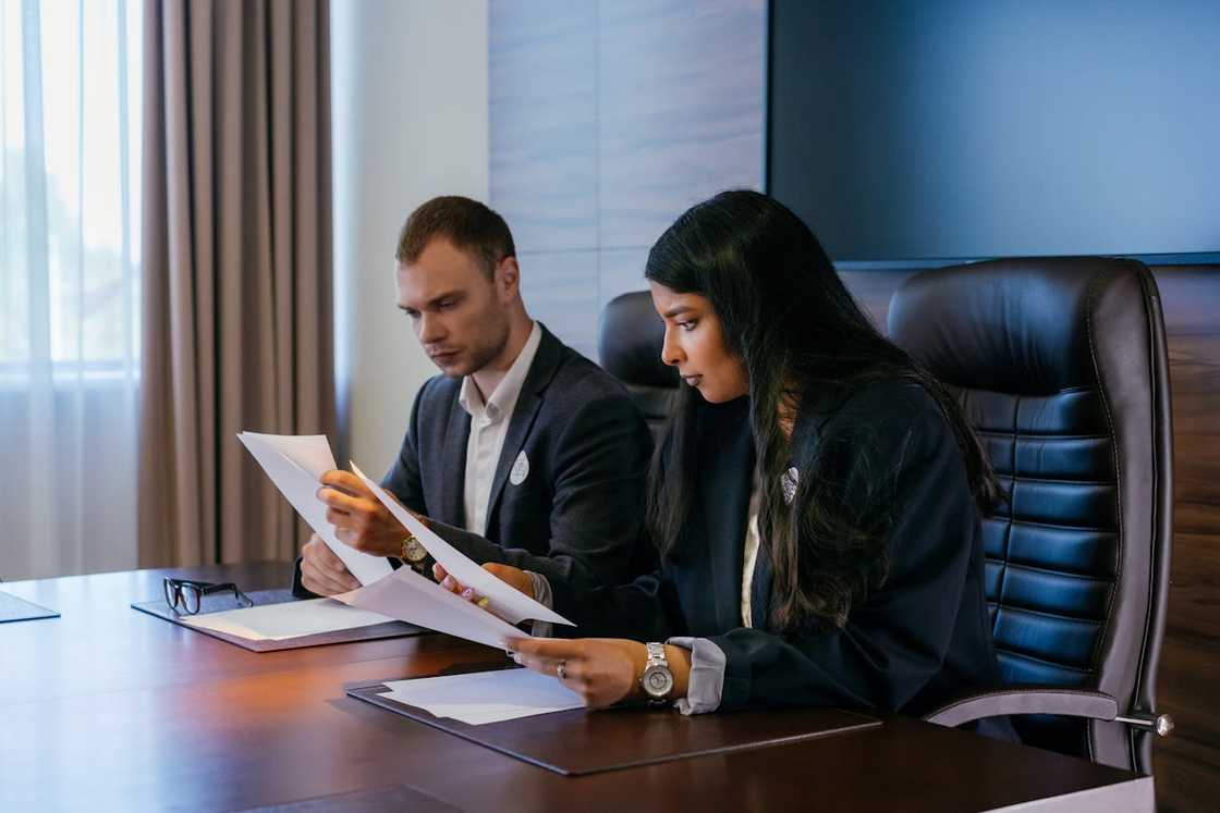 Two lawyers closely reviewing printed documents during a formal meeting. Two lawyers closely reviewing printed documents during a formal meeting.