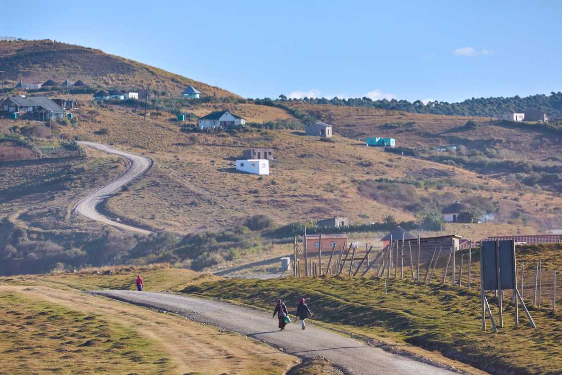 Local village women walk along a road towards the homesteads Local village women walk along a road towards the homesteads
