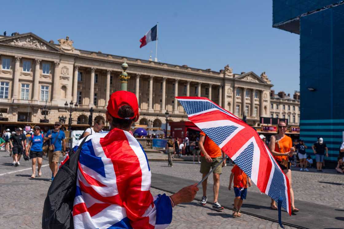 A spectator wrapped in a British Union flag shelters from the sun with an umbrella