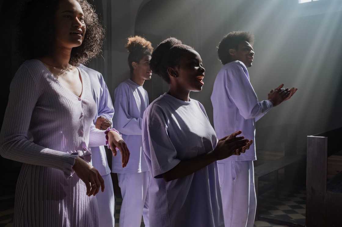 A group of people sing together inside a church with sunlight streaming in.