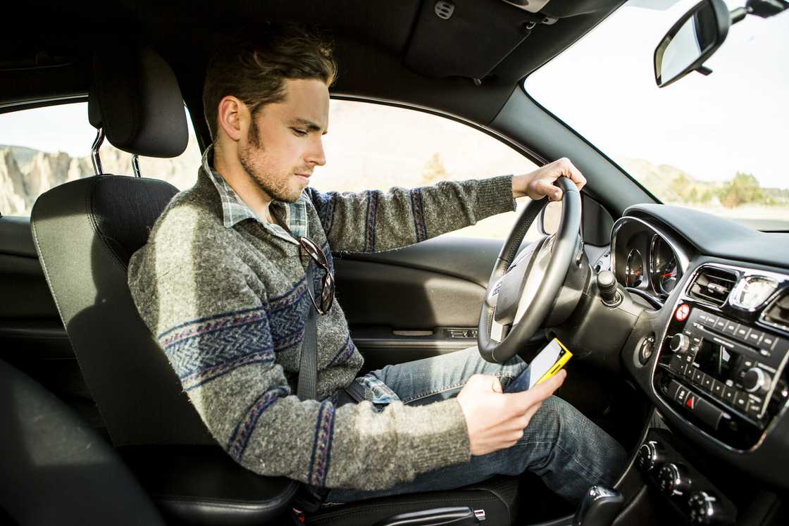 A motorist looks at his phone while sitting in his car. A motorist looks at his phone while sitting in his car.