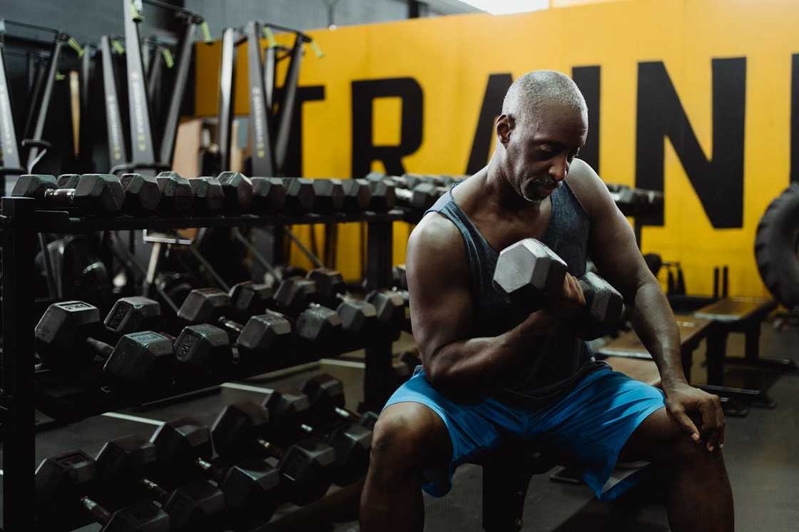 A man lifts a dumbbell while seated in a gym surrounded by weights.