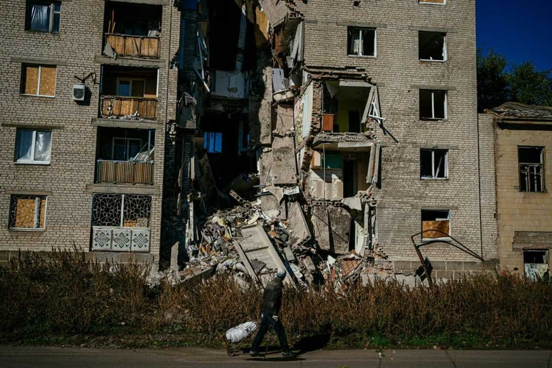 In a devastated part of Bakhmut, where many buildings are gutted, neighbours go and charge their phones in a shop where there is a generator