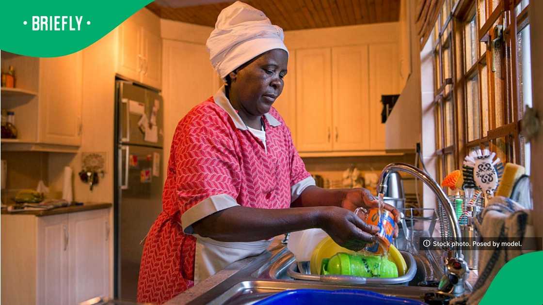 The photograph captured a woman carefully rinsing kitchenware under running water with household cabinets and a refrigerator visible in the background
