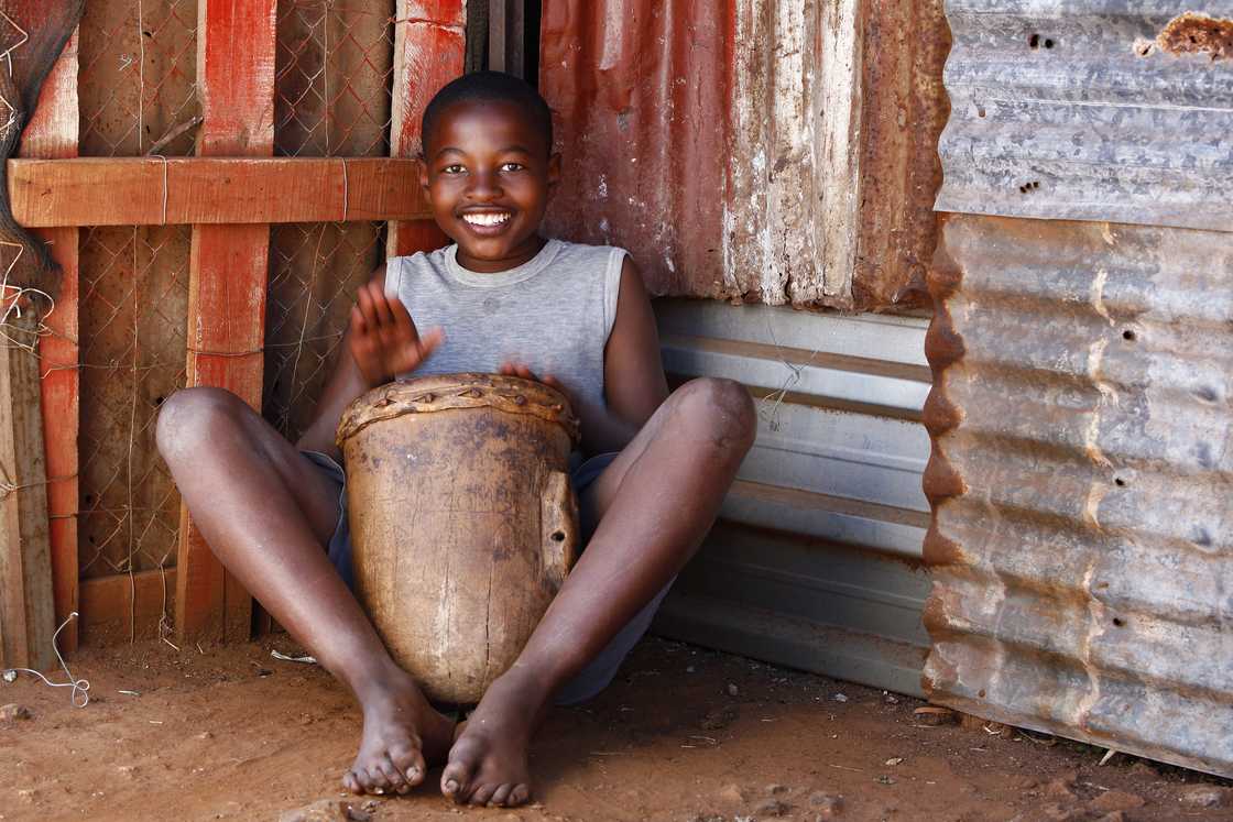 A barefoot child smiling while playing a traditional drum. A barefoot child smiling while playing a traditional drum.