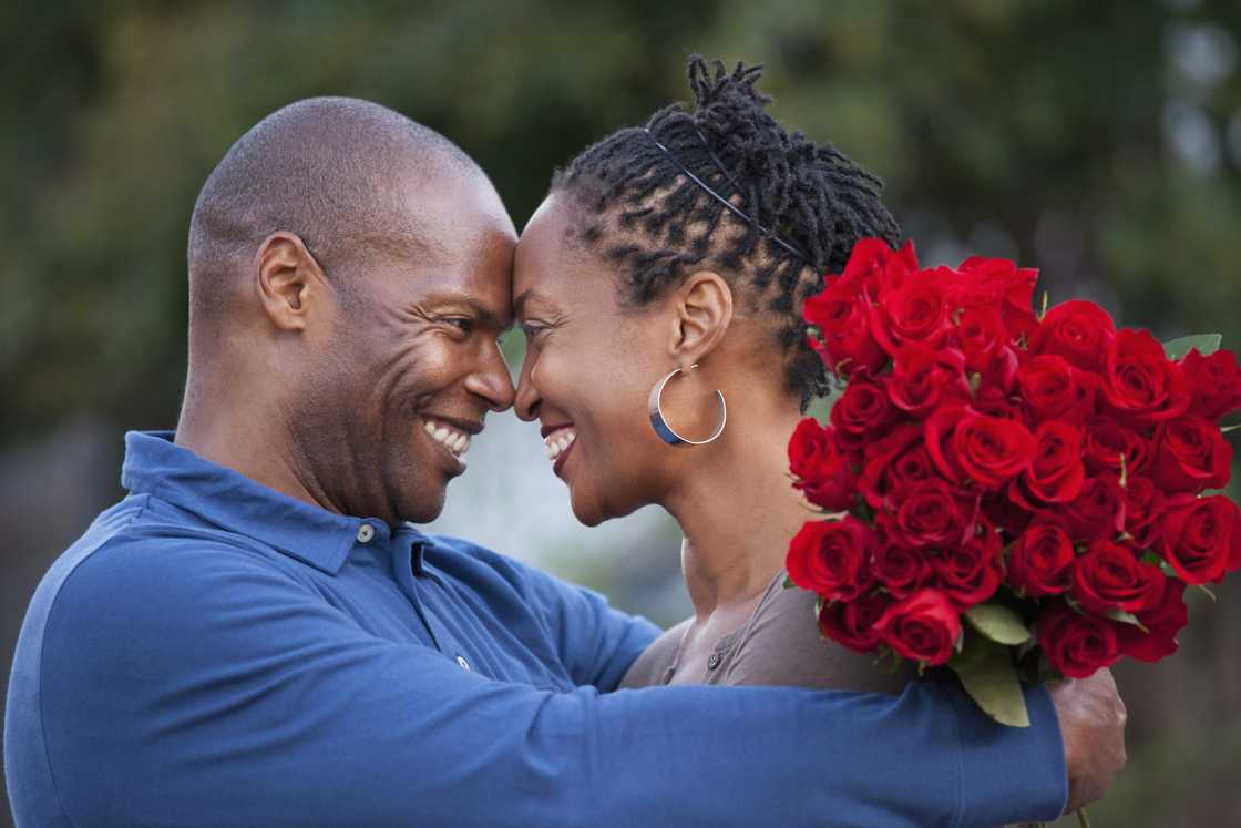 A man hugging wife and giving her red roses.