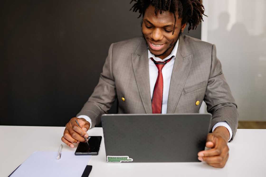 A man smiles while working on a laptop at a desk. A man smiles while working on a laptop at a desk.