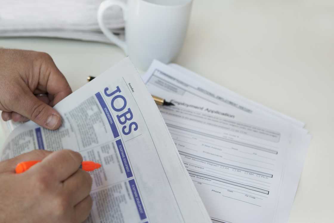 A stock photo of close-up of hands searching for jobs in newspaper with cup in background
