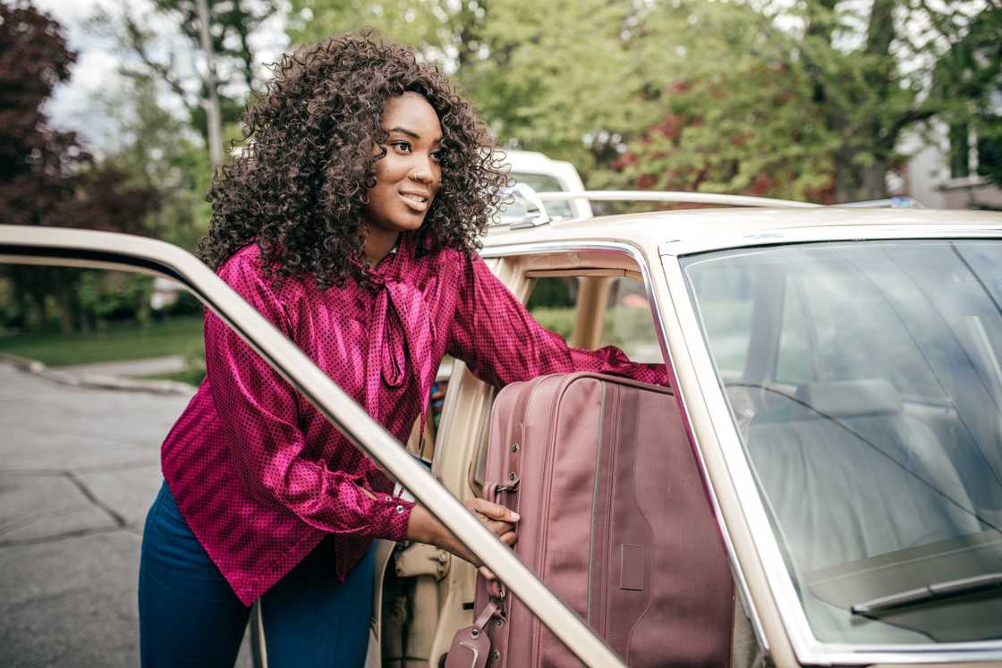 A woman loading suitcase into ride-share car.