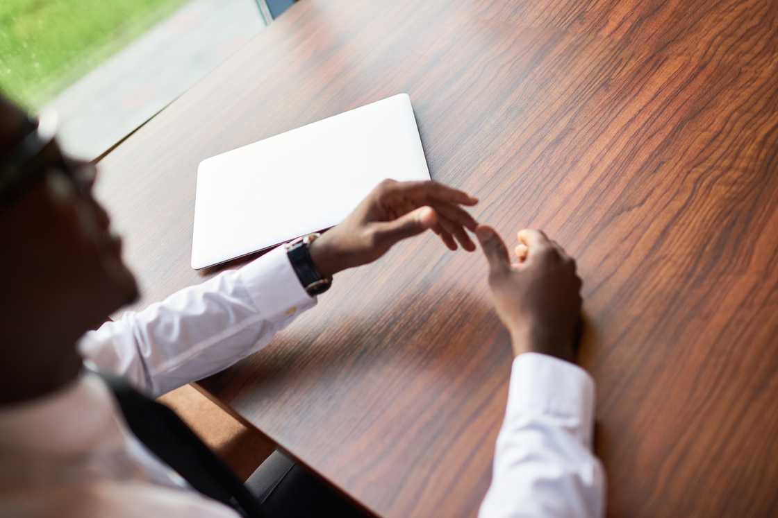 A hand adjusts a cufflink beside a brown envelope on a desk. A hand adjusts a cufflink beside a brown envelope on a desk.