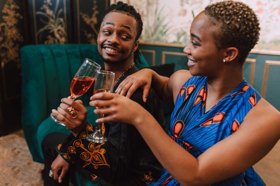 A man and a woman sit close together on a sofa, smiling and holding drinks.
