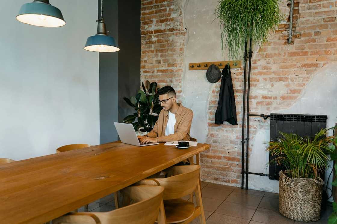 A man in brown long sleeves using his laptop while sitting near the wooden table