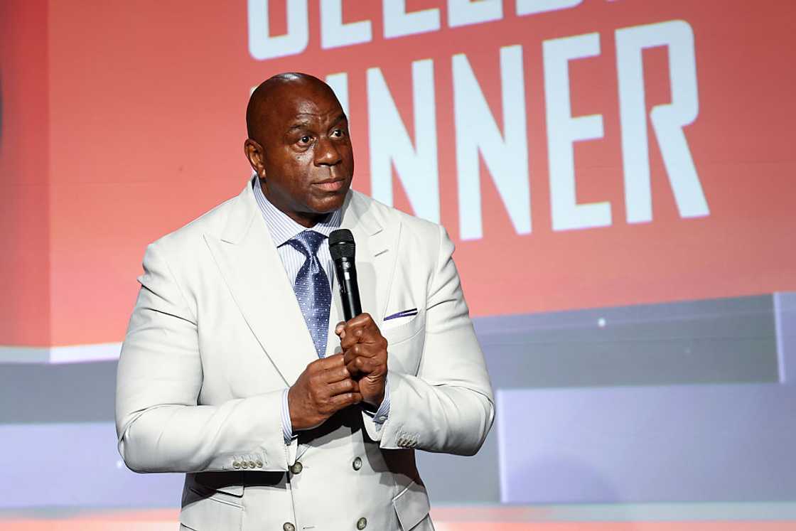 Magic Johnson in a white suit speaking onstage at the Harold and Carole Pump Foundation 25th Anniversary Celebrity Dinner