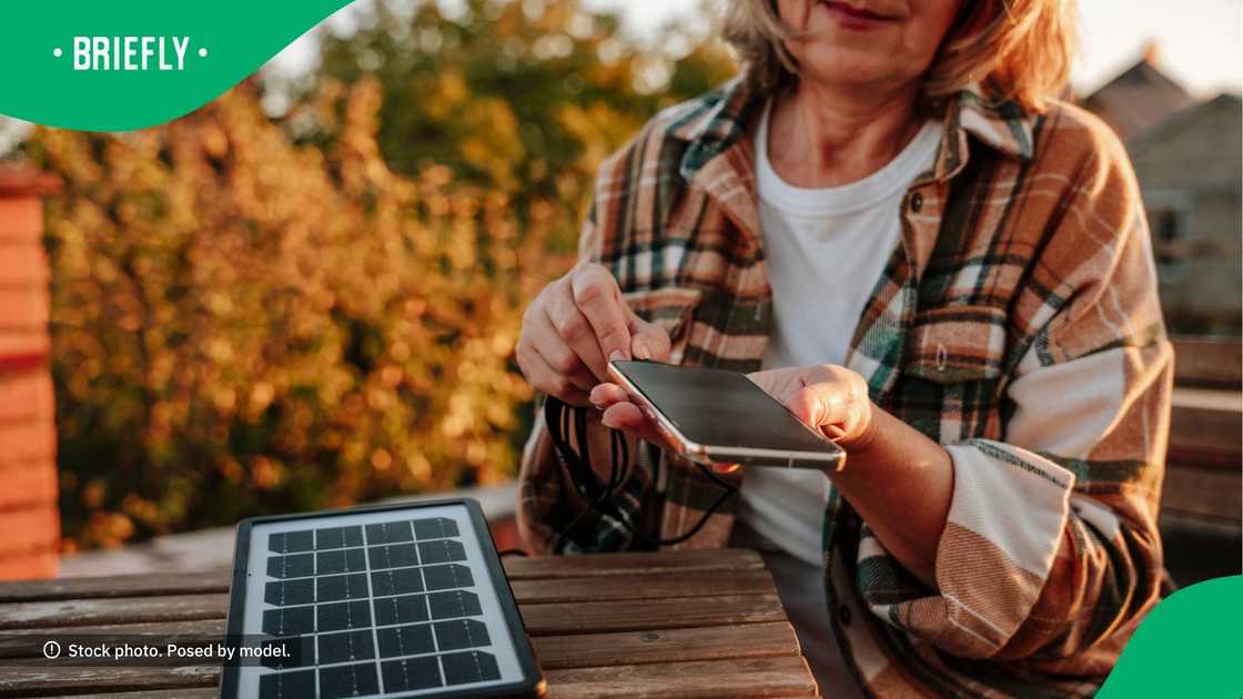 A woman charging her phone using a solar panel.