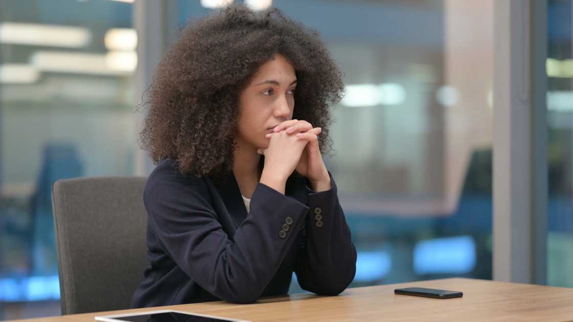 Person sits at a conference table with hands clasped near face.