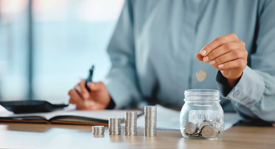 Investment, finance and savings of a business accountant stacking silver, currency or coins with hand and money closeup indoor. One wise smart person planning a financial budget in growth jar concept Investment, finance and savings of a business accountant stacking silver, currency or coins with hand and money closeup indoor. One wise smart person planning a financial budget in growth jar concept
