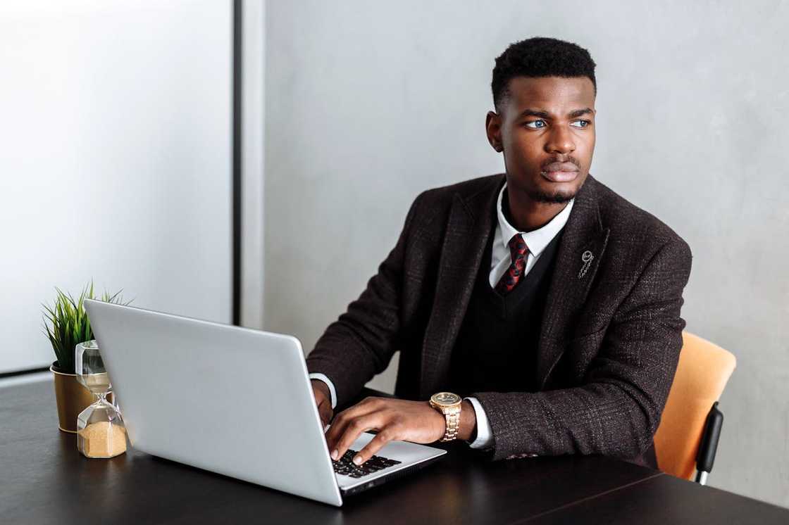 A man in a business attire working on a laptop at a desk. A man in a business attire working on a laptop at a desk.