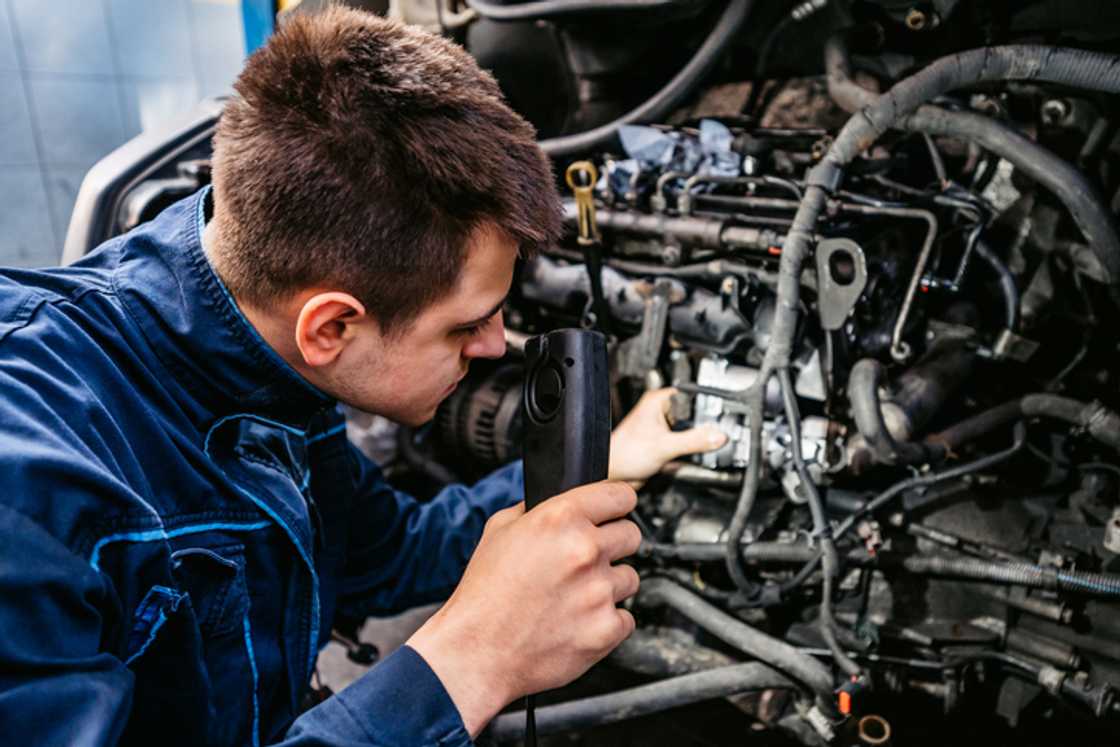 An auto mechanic fixing a car with a lamp in mechanics garage An auto mechanic fixing a car with a lamp in mechanics garage