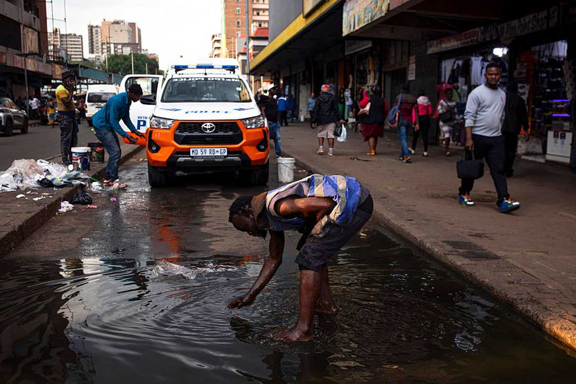 A homeless person washes himself in a flooded water in a busy market area on November 12, 2025 in central Johannesburg, South Africa. Johannesburg, historically known as the City of Gold, is facing challenges including aging infrastructure. A homeless person washes himself in a flooded water in a busy market area on November 12, 2025 in central Johannesburg, South Africa. Johannesburg, historically known as the City of Gold, is facing challenges including aging infrastructure.
